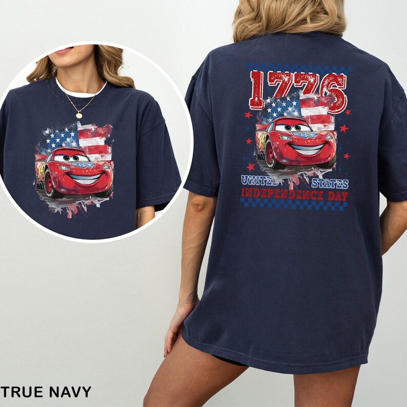 May include: A navy blue t-shirt featuring a graphic of a red race car with eyes on the windshield, set against a stylised American flag. The back print includes the text 1776, UNITED STATES, and INDEPENDENCE DAY in red, white, and blue colours.