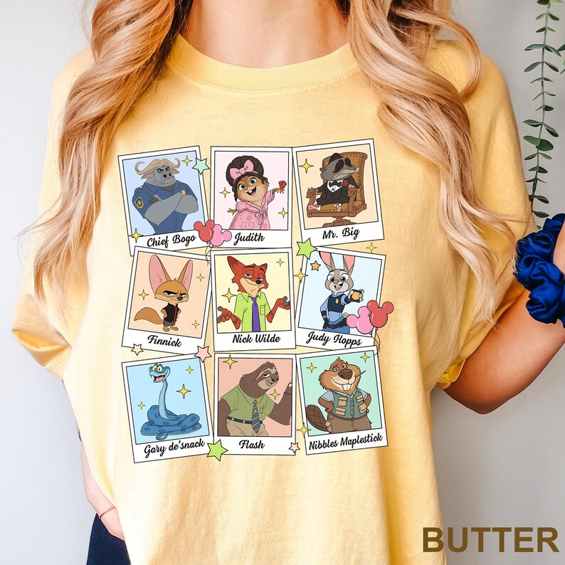 Op de afbeelding: Een lichtgeel t-shirt met een raster van negen frames in polaroidstijl. Elk frame bevat een stripfiguur met de naam eronder gedrukt: Chief Bogo, Judith, Mr. Big, Finnick, Nick Wilde, Judy Hopps, Gary de'snack, Flash en Nibbles Maplestick.