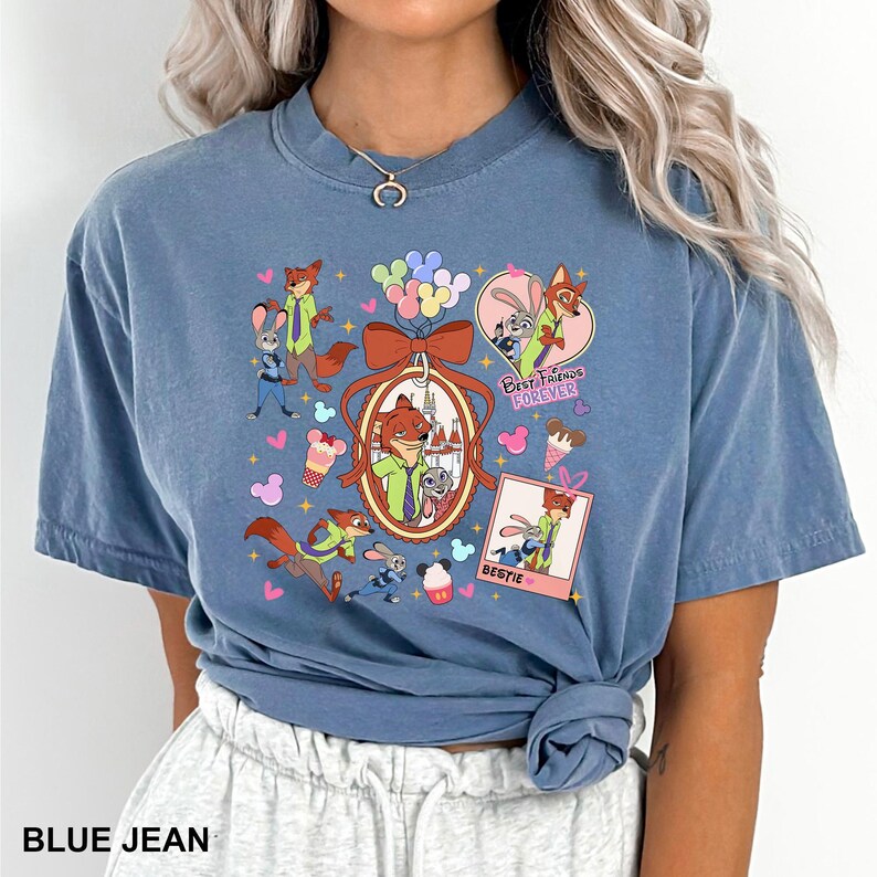 Op de afbeelding: Blauw spijkerbroekkleurig T-shirt met een kleurrijke afbeelding van stripfiguren, waaronder een vos en een konijn, met de tekst "Best Friends Forever" en "Bestie". Het ontwerp bevat harten, ballonnen en ijsjes.