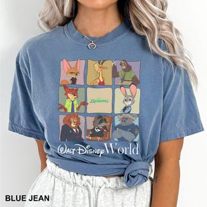 May include: Blue jean-colored t-shirt featuring a grid of Zootopia characters. The shirt has the words "Walt Disney World" printed below the grid. The shirt is a short-sleeved, crew neck style.
