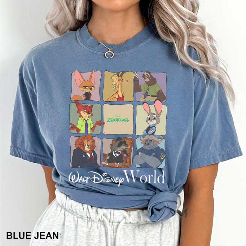 May include: Blue jean-colored t-shirt featuring a grid of Zootopia characters. The shirt has the words "Walt Disney World" printed below the grid. The shirt is a short-sleeved, crew neck style.