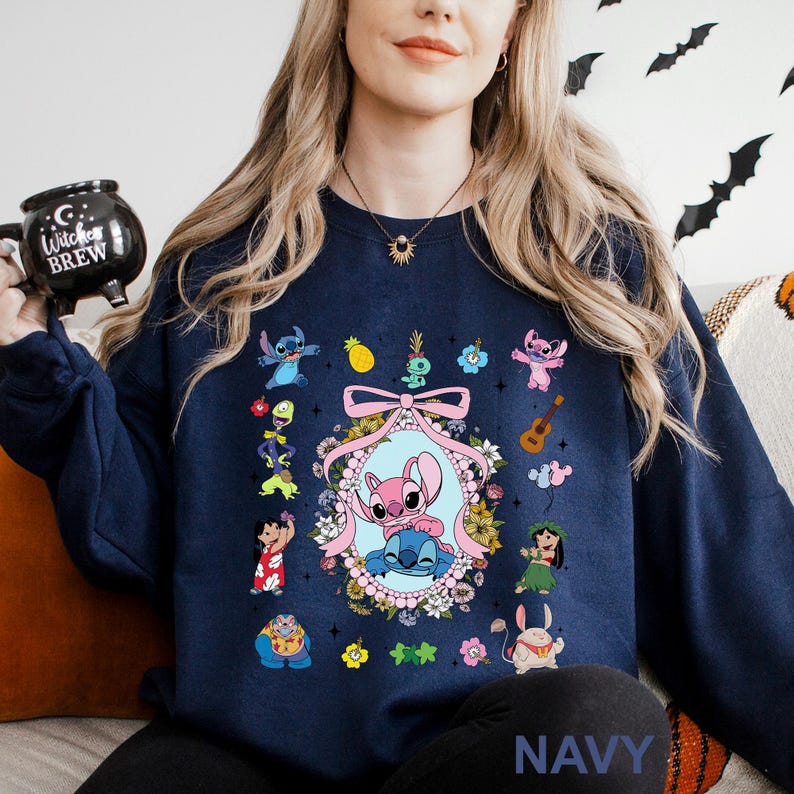 May include: Navy blue sweatshirt featuring a colorful graphic of the characters Stitch and Angel, surrounded by floral and tropical elements. The design includes a central oval frame with the characters, and smaller character illustrations around the frame. The word "NAVY" is at the bottom.