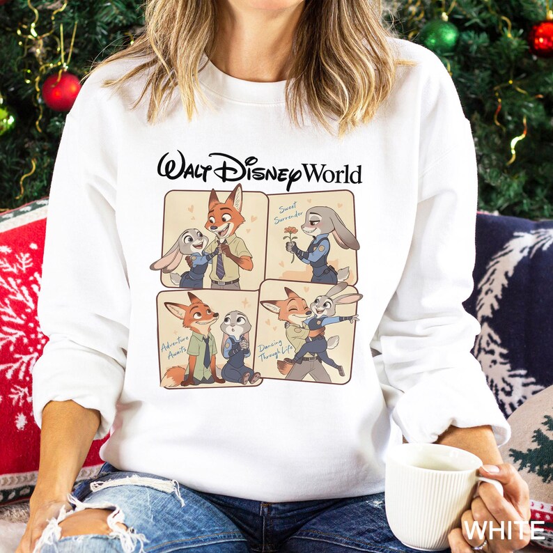 May include: White sweatshirt featuring a Walt Disney World graphic with cartoon images of Nick Wilde and Judy Hopps. The graphic includes the phrases "Sweet Surrender", "Adventure Awaits", and "Dancing Through Life". The sweatshirt is made of a soft material.