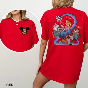 May include: Red t-shirt featuring a Mickey Mouse police badge on the front and a cartoon illustration on the back. The back design includes characters like Judy Hopps and Nick Wilde, with the text "Judy", "Nick", and "Nibbles".