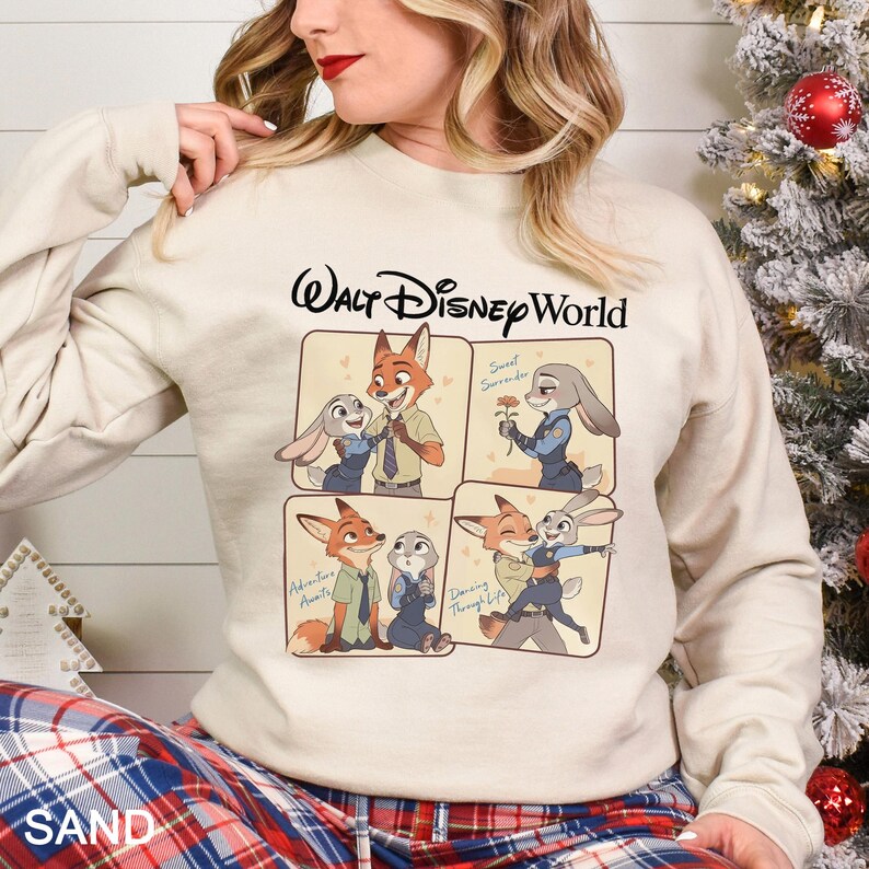 May include: A sand-colored sweatshirt featuring a Walt Disney World logo and four panels with illustrations of Nick Wilde and Judy Hopps from Zootopia. The illustrations depict various scenes of the characters together. The sweatshirt is made of a soft material.