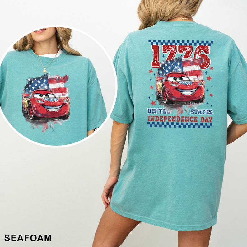 May include: A seafoam green t-shirt featuring a graphic of a red race car in front of an American flag. The back print includes the text 1776 and UNITED STATES INDEPENDENCE DAY with a blue and white checkered border and red stars.