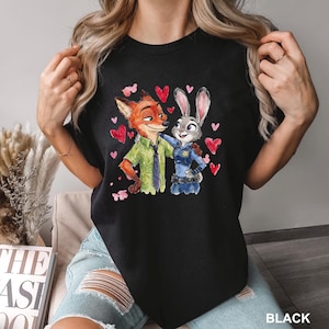 Może przedstawiać: Czarny t-shirt z akwarelową ilustracją Nicka Wilde'a i Judy Hopps z filmu Zwierzogr&oacute;d, otoczonych czerwonymi sercami. Tekst "BLACK" jest wydrukowany w prawym dolnym rogu.