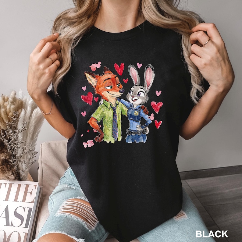 Może przedstawiać: Czarny t-shirt z akwarelową ilustracją Nicka Wilde'a i Judy Hopps z filmu Zwierzogr&oacute;d, otoczonych czerwonymi sercami. Tekst "BLACK" jest wydrukowany w prawym dolnym rogu.