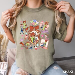 Op de afbeelding: Khaki T-shirt met een kleurrijke afbeelding van cartoon vos- en konijnfiguren. Het ontwerp bevat de tekst "Best Friends Forever" en "Bestie". Het shirt heeft een ronde hals en korte mouwen.