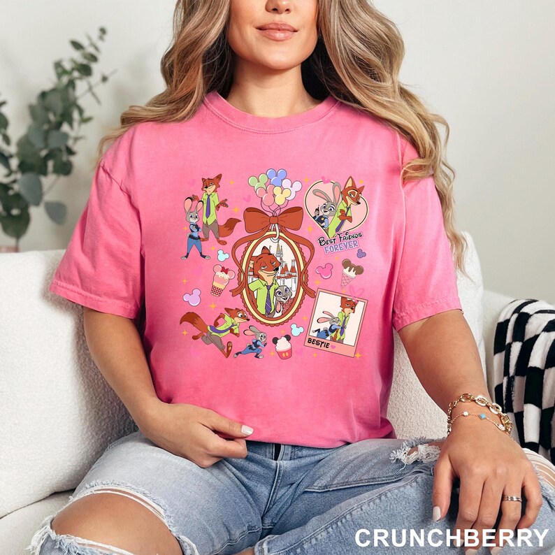 Op de afbeelding: Roze T-shirt met een kleurrijke afbeelding van personages uit de animatiefilm Zootopia. Het ontwerp bevat de tekst "Best Friends Forever" en "Bestie". Het shirt heeft een ronde hals en korte mouwen.