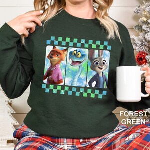 May include: Forest green sweatshirt featuring a graphic of three animated characters in a film strip design. The characters include a fox, a snake, and a rabbit. The sweatshirt has long sleeves and the text "FOREST GREEN" is visible.