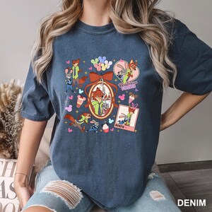 Op de afbeelding: Een denim blauw t-shirt met een kleurrijke afbeelding van stripfiguren, waaronder een vos en een konijn, met de tekst "Best Friends Forever" en "Bestie". Het ontwerp bevat harten, ballonnen en ijsjes.
