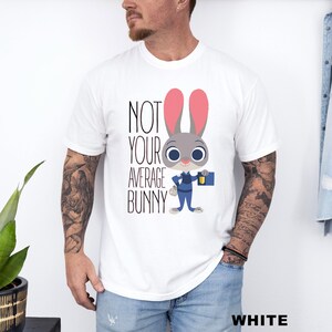 May include: White t-shirt featuring the text "NOT YOUR AVERAGE BUNNY" and a cartoon bunny character. The bunny is grey with pink ears, wearing a blue uniform and holding a blue briefcase. The word "WHITE" is at the bottom.