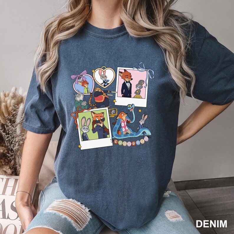 May include: A dark blue t-shirt with a colourful graphic of Zootopia characters. The design includes framed images of the characters, with the word "Zootopia" at the bottom. The shirt is a casual wear item.