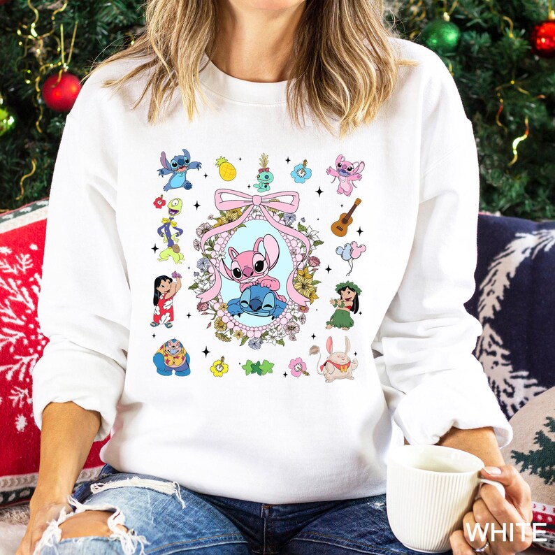 May include: White sweatshirt featuring a colorful graphic of Stitch and other characters. The design includes a pink bow, floral frame, and various cartoon elements. The sweatshirt is a casual style.
