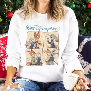 Puede incluir: Sudadera blanca con un gr&aacute;fico de Walt Disney World con im&aacute;genes de dibujos animados de un zorro y un conejo. Las palabras "Walt Disney World" est&aacute;n en azul claro. La palabra "WHITE" est&aacute; en la esquina inferior derecha.