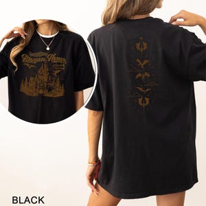 May include: Black t-shirt with a gold graphic on the front featuring a castle, trees, and the text "Riccon House". The back of the shirt has a gold design of dragons and clouds. The word "BLACK" is at the bottom of the image.