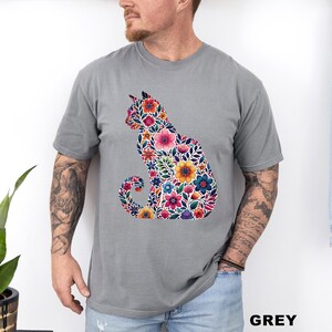 May include: A grey t-shirt featuring a floral cat silhouette. The cat design is filled with colorful flowers in shades of pink, yellow, blue, and orange. The word "GREY" is printed in the bottom right corner of the image.