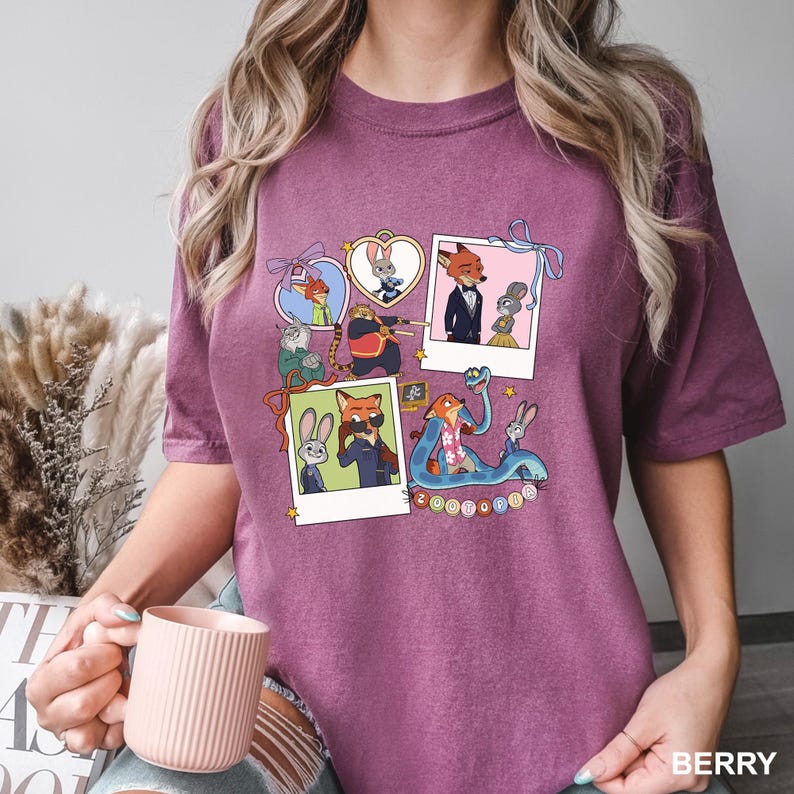 May include: Berry-coloured t-shirt with a colourful graphic of Zootopia characters. The design includes multiple framed images of the characters, with the word "Zootopia" at the bottom. The shirt is made of a soft material.
