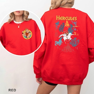 K&ouml;nnte beinhalten: Roter Sweatshirt mit einem Cartoon-Motiv von Herkules auf der Vorderseite und einer gr&ouml;&szlig;eren Grafik auf der R&uuml;ckseite. Die R&uuml;ckengrafik enth&auml;lt das Wort "Hercules" in Gelb sowie verschiedene Charakterillustrationen in Blau und Wei&szlig;.
