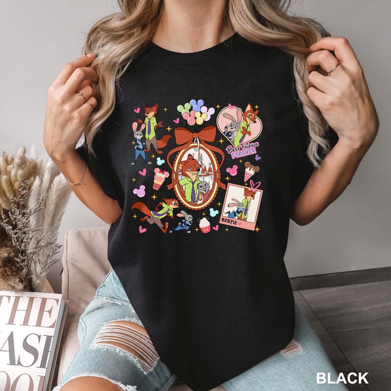 Op de afbeelding: Zwart T-shirt met een kleurrijk grafisch ontwerp met stripfiguren, waaronder een vos en een konijn. Het ontwerp bevat de tekst "Best Friends Forever" en "Bestie". Het shirt heeft een ronde hals.