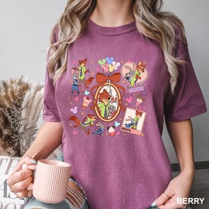 Op de afbeelding: Bessenkleurig T-shirt met stripfiguren uit Zootopia. Het ontwerp bevat Nick Wilde en Judy Hopps, met de tekst "Best Friends Forever" en "Bestie". Het shirt heeft een ronde hals en korte mouwen.