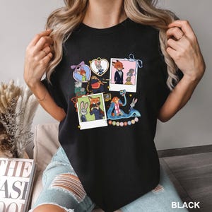 May include: Black crew neck t-shirt with colourful cartoon images of Zootopia characters. The graphic includes Nick Wilde, Judy Hopps, and other characters in various poses. The word "BLACK" is printed at the bottom right of the t-shirt.