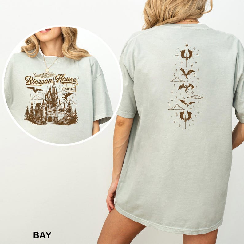 May include: A light green t-shirt with a brown graphic of a castle, trees, and dragons. The text "Riorrson House" is above the castle. The back of the shirt has a vertical design of dragons and clouds.