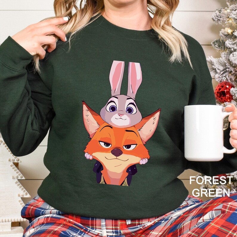 Pode incluir: Camisola verde floresta com uma imagem de desenho animado de uma raposa e um coelho. A raposa &eacute; laranja e o coelho &eacute; cinzento. O texto "FOREST GREEN" est&aacute; impresso no canto inferior direito da imagem.