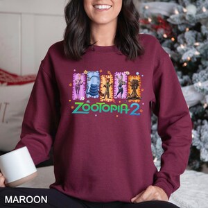 Puede incluir: Sudadera granate con el texto "ZOOTOPIA 2" e ilustraciones de personajes. El dise&ntilde;o incluye im&aacute;genes de Judy Hopps, Nick Wilde y otros personajes de la pel&iacute;cula animada. La sudadera es de color granate liso.
