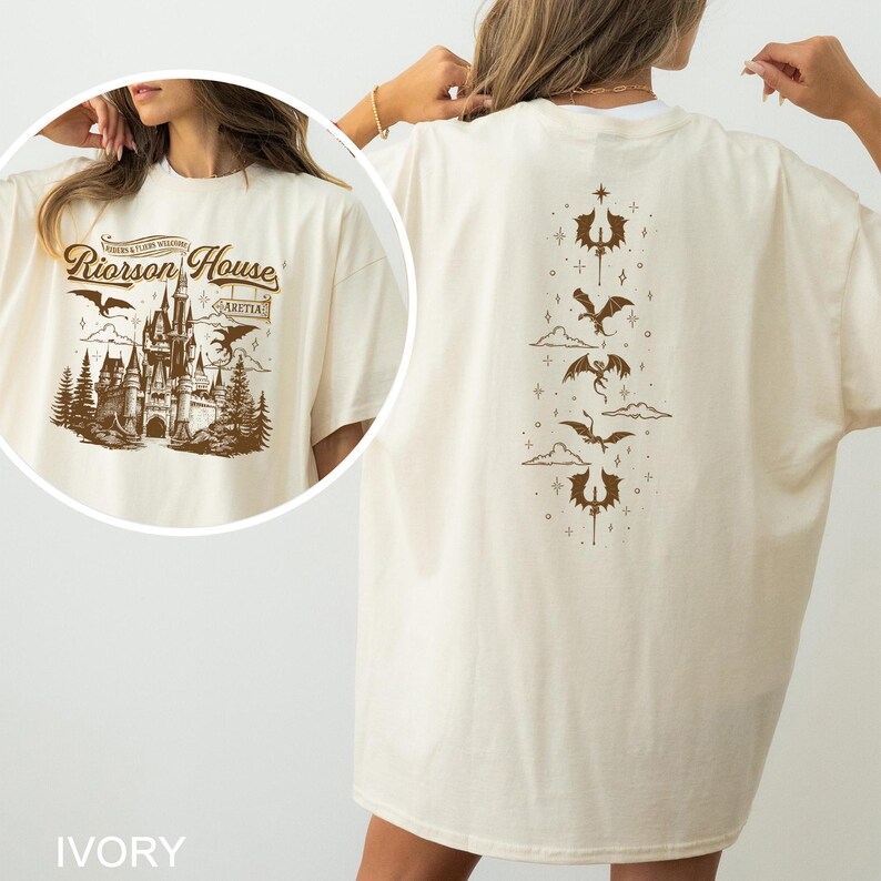 May include: Ivory-colored t-shirt featuring a brown graphic of a castle with the text "Riorrson House" on the front. The back of the shirt displays a vertical design of dragons and decorative elements. The shirt is a relaxed fit.