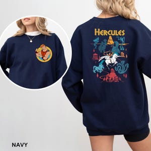K&ouml;nnte beinhalten: Marineblaues Sweatshirt mit einer farbenfrohen Grafik von Herkules auf dem R&uuml;cken und einem kleineren Bild auf der Vorderseite. Das Design auf der R&uuml;ckseite enth&auml;lt das Wort "Hercules" &uuml;ber einer Szene mit Figuren aus dem Zeichentrickfilm. Die Vorderseite hat ein rundes Bild von Herkules.