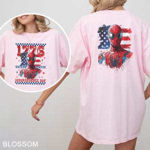Może przedstawiać: Jasnor&oacute;żowy t-shirt z grafiką Spider-Mana na tle postarzałej amerykańskiej flagi. Przedni wz&oacute;r zawiera napis 1776 UNITED STATES INDEPENDENCE DAY. Tylny wz&oacute;r przedstawia większą wersję tej samej postaci w podobnym stylu graficznym.