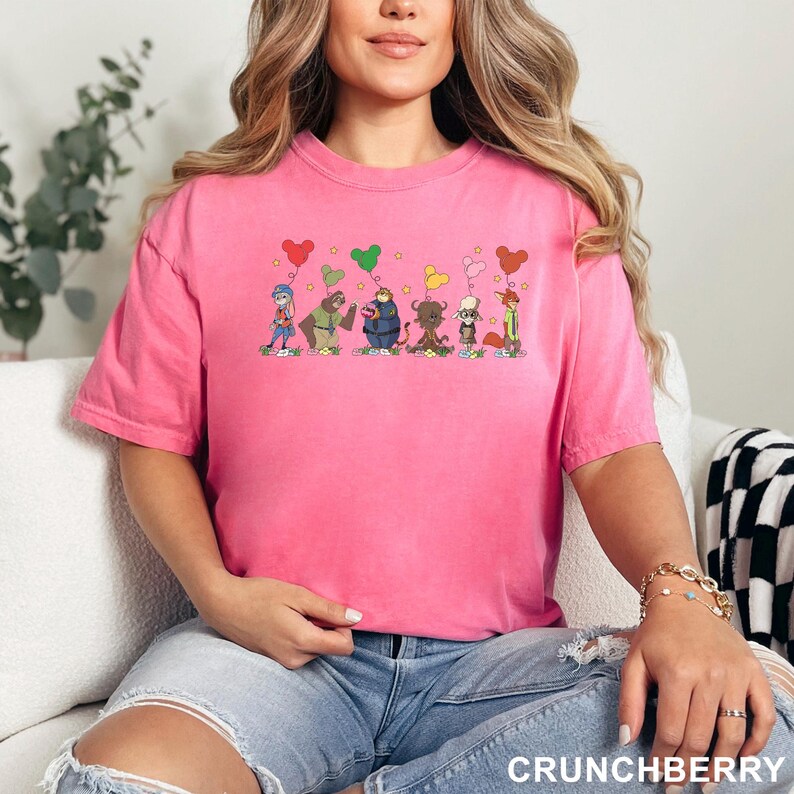 May include: A hot pink t-shirt featuring a cartoon graphic of several whimsical characters holding heart-shaped balloons. The word "CRUNCHBERRY" is printed in white at the bottom of the image. The shirt is made of a soft material.