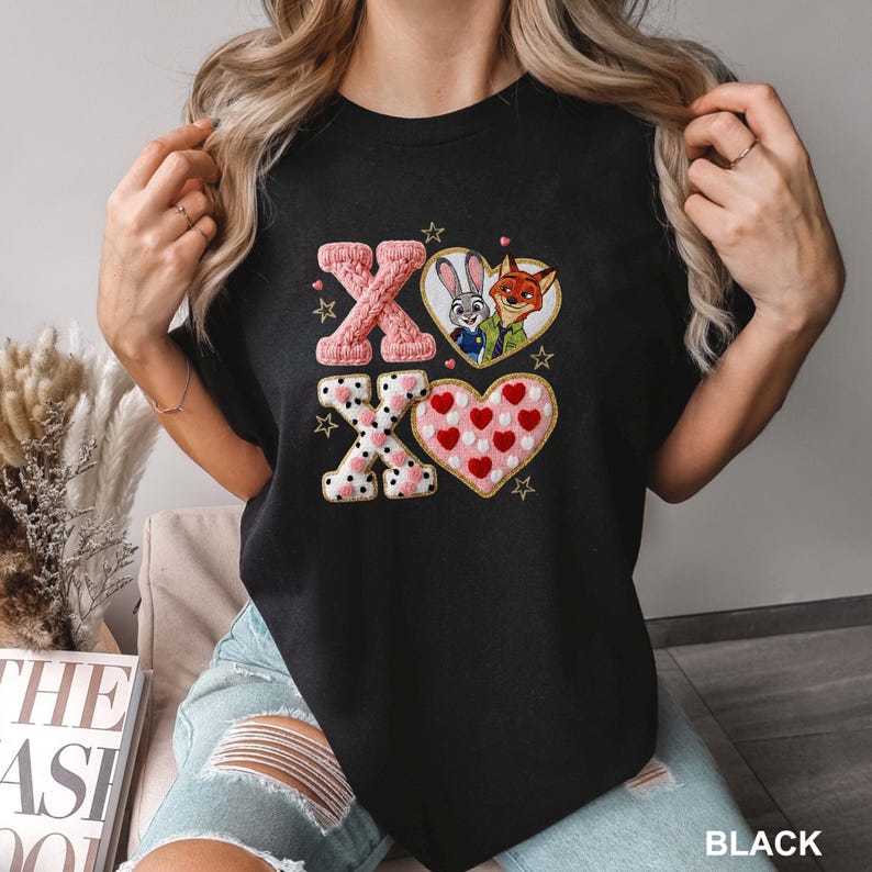 Może przedstawiać: Czarny t-shirt z haftowanym wzorem "XO". Projekt zawiera r&oacute;żowe dzianinowe litery, serce z Judy Hopps i Nickiem Wilde oraz serce wypełnione czerwonymi sercami. Złote gwiazdy zdobią projekt.