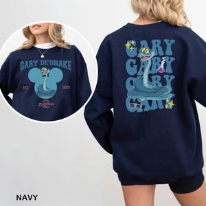 May include: Navy blue sweatshirt featuring a cartoon snake character with the text "GARY DE'SNAKE" and "ZOOTOPIA" on the front. The back of the sweatshirt has a vertical design with the name "GARY" repeated and the snake character. The sweatshirt has a crew neck.