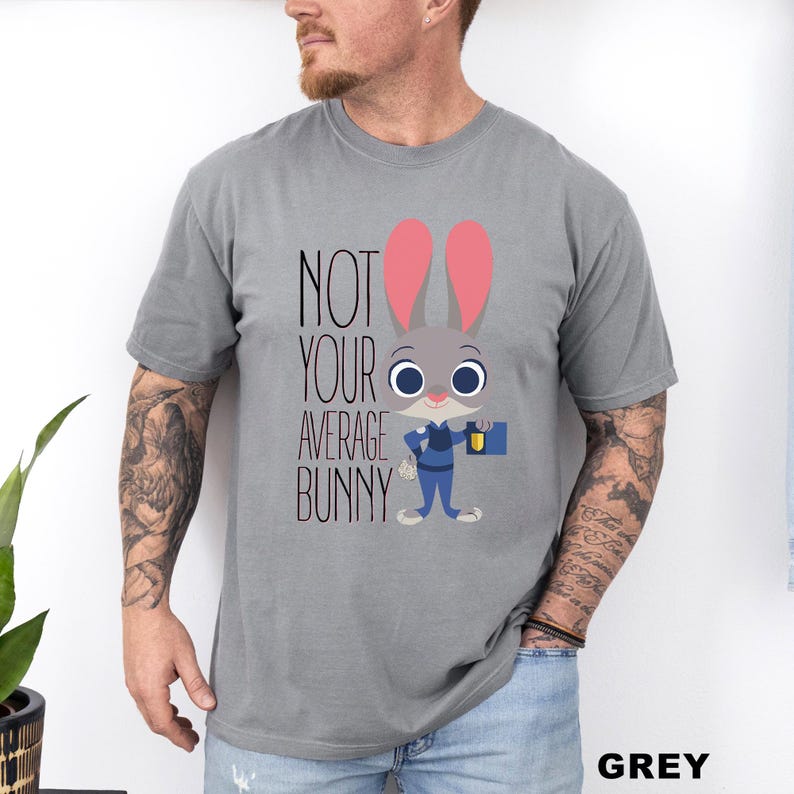 May include: A grey t-shirt with a cartoon bunny in a police uniform, holding a briefcase. The text "NOT YOUR AVERAGE BUNNY" is printed above the bunny. The word "GREY" is printed at the bottom right corner of the shirt.