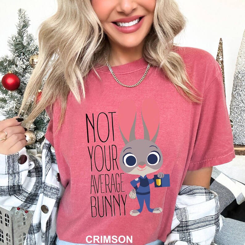 May include: Crimson t-shirt featuring the text "NOT YOUR AVERAGE BUNNY" and a cartoon bunny character in a blue uniform, holding a case. The shirt is a short-sleeved crew neck. The word "CRIMSON" is at the bottom.