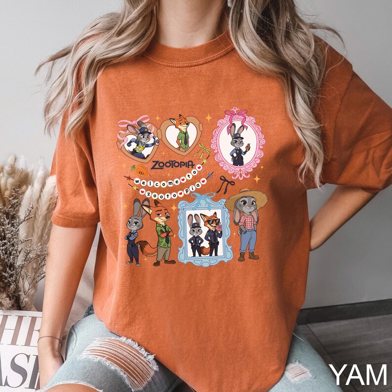 Op de afbeelding: Verbrand oranje t-shirt met een kleurrijke afbeelding van personages uit de animatiefilm Zootopia. Het ontwerp bevat ingelijste portretten van de personages, het woord "Zootopia" en het woord "Welcome" in een kralenketting.