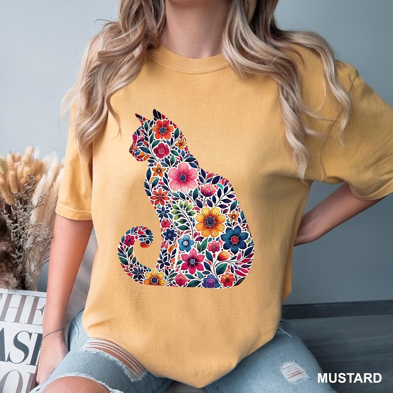 May include: Mustard-colored t-shirt featuring a floral cat design. The cat silhouette is filled with colorful flowers, leaves, and intricate details. The word "MUSTARD" is printed in white at the bottom right corner of the image.