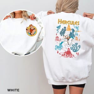 K&ouml;nnte beinhalten: Wei&szlig;es Sweatshirt mit einer Cartoon-Illustration von Herkules auf dem R&uuml;cken, mit dem Wort "Hercules" in goldfarbenen Buchstaben. Auf der Vorderseite befindet sich eine kleinere kreisf&ouml;rmige Grafik von Herkules. Auf der Unterseite des Sweatshirts steht das Wort "WHITE".