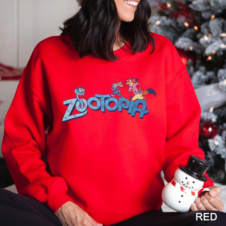 May include: A vibrant red sweatshirt with the word "Zootopia" in blue, and cartoon characters. The sweatshirt has long sleeves and a crew neck. The word "RED" is in the bottom right corner.