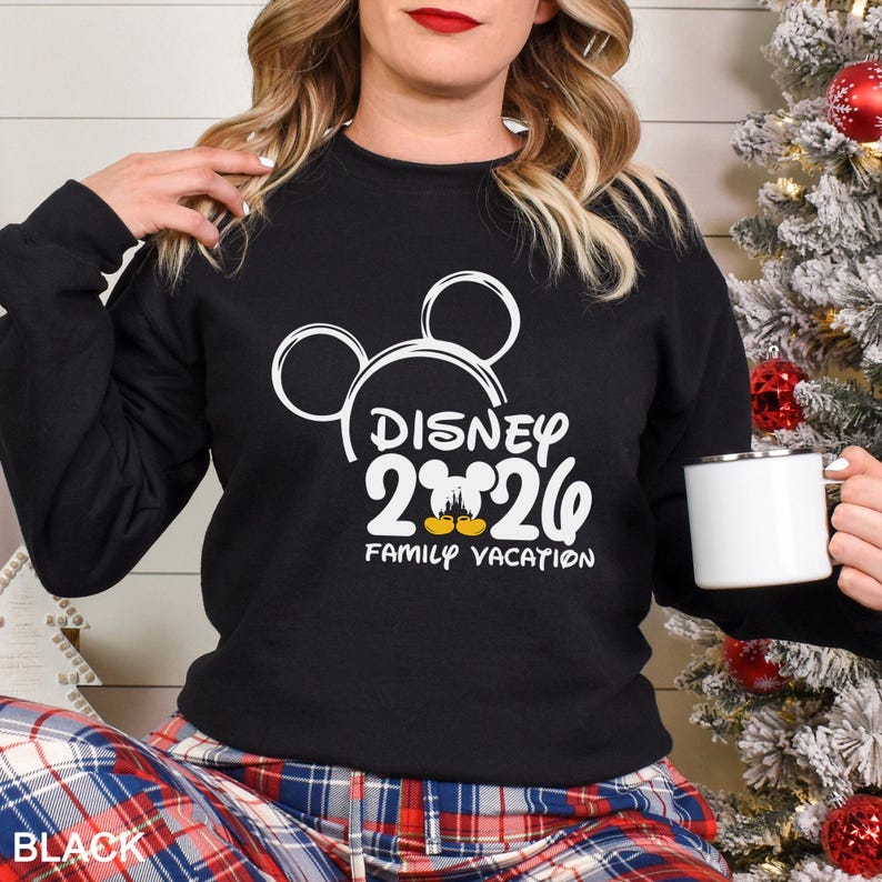 以下が含まれることがあります： 白のディズニー2020グラフィックと「Family Vacation」の文字が入った黒のクルーネックのトレーナー。トレーナーにはミッキーマウスの耳が付いています。「BLACK」の文字が左下に印刷されています。