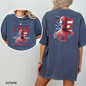Może przedstawiać: Ciemnoniebieski t-shirt z grafiką Spider-Mana na tle postarzałej amerykańskiej flagi. Przedni wz&oacute;r zawiera napis 1776 UNITED STATES INDEPENDENCE DAY, natomiast na plecach znajduje się większa wersja tej samej grafiki z postacią superbohatera.