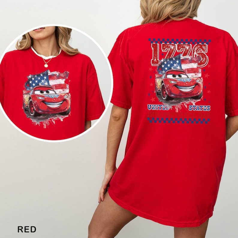 May include: A bright red t-shirt featuring a graphic of a red race car with eyes on the windscreen, set against a stylised American flag. The back design includes the text 1776 and UNITED STATES, framed by a blue and red chequered border.