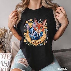 Peut inclure: T-shirt noir avec un motif color&eacute; des personnages de Zootopie, Judy Hopps et Nick Wilde, en uniforme de police, entour&eacute;s de fleurs et d'un badge dor&eacute; avec l'inscription "POLICE". Le mot "BLACK" est imprim&eacute; en bas.