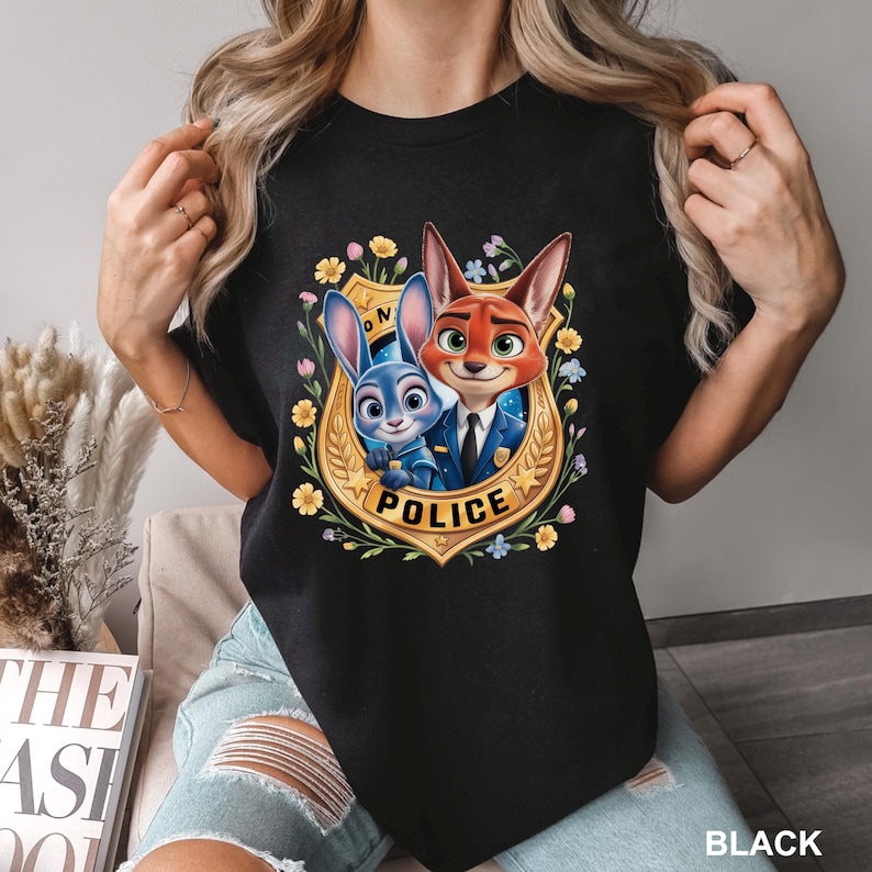 Peut inclure: T-shirt noir avec un motif color&eacute; des personnages de Zootopie, Judy Hopps et Nick Wilde, en uniforme de police, entour&eacute;s de fleurs et d'un badge dor&eacute; avec l'inscription "POLICE". Le mot "BLACK" est imprim&eacute; en bas.