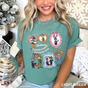 Op de afbeelding: Lichtgroen T-shirt met een Zootopia-ontwerp. Het ontwerp bevat ingelijste afbeeldingen van personages, het woord "Zootopia" en andere decoratieve elementen. Het T-shirt is effen lichtgroen van kleur.