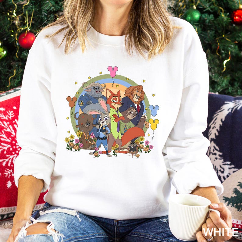 May include: White crewneck sweatshirt featuring a colorful graphic of animated animal characters. The design includes a rainbow, flowers, and Mickey Mouse-shaped balloons. The sweatshirt is made of a soft material.