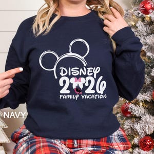 以下が含まれることがあります： 白のミッキーマウスの輪郭と「DISNEY 2026 FAMILY VACATION」の文字が入ったネイビーブルーのスウェットシャツ。スウェットシャツは長袖とクルーネックです。「NAVY」の文字が左下にプリントされています。